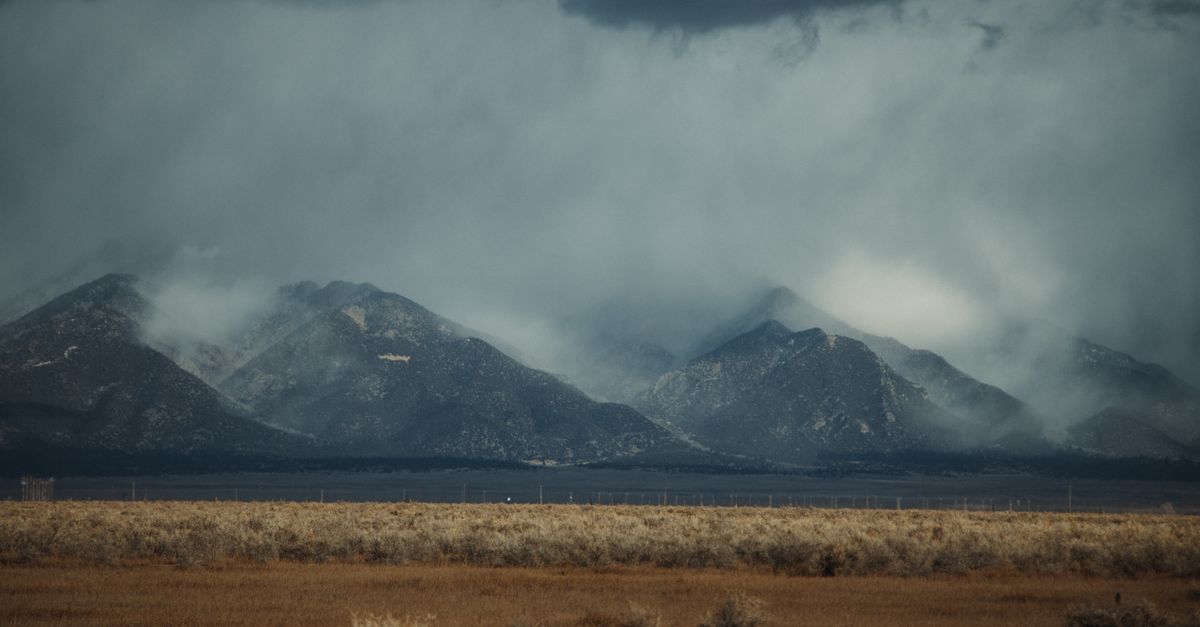 Atmospheric shot of mountains shrouded in winter clouds with a vast foreground, conveying a moody and dramatic vibe.