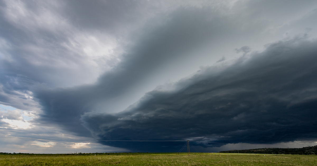 Dramatic storm clouds gather over a lush green field, signaling an approaching thunderstorm in KwaZulu-Natal.