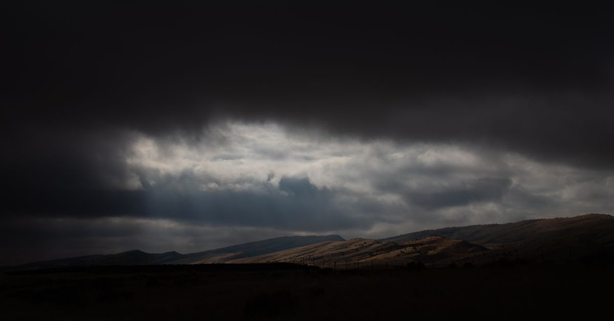Moody clouds with sun rays over a darkened, vast rural landscape.