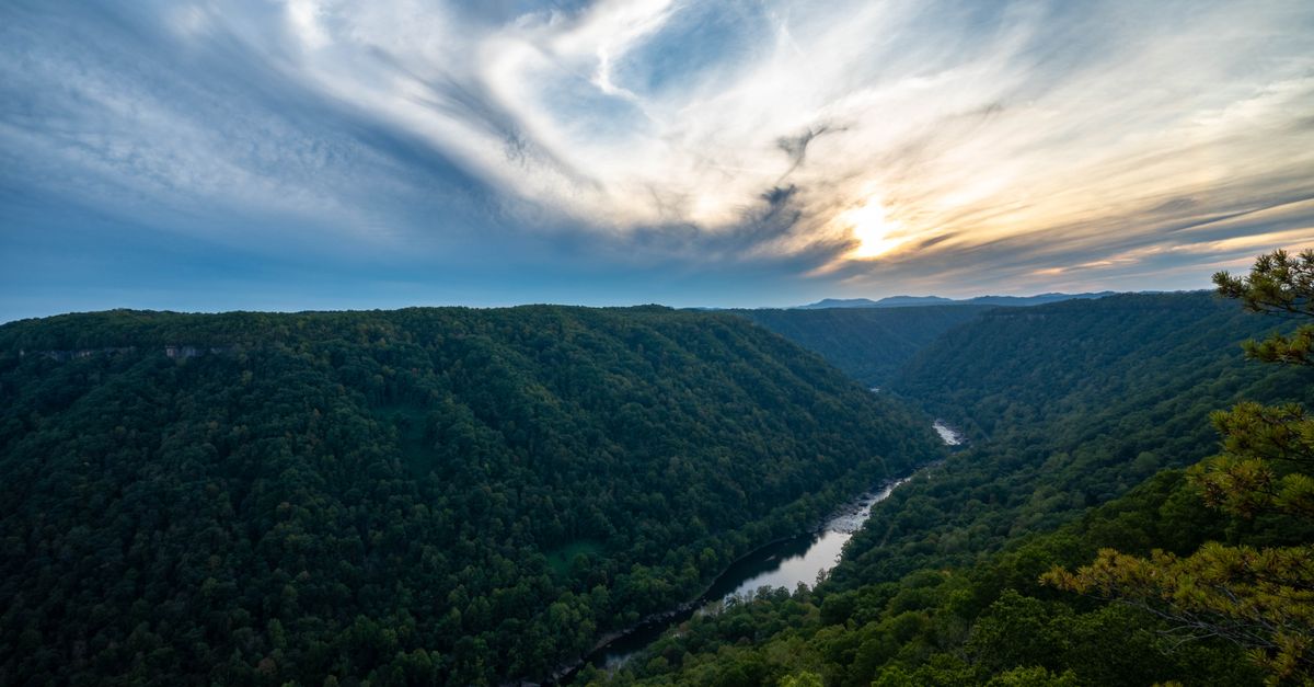 A breathtaking view of a river winding through lush green hills beneath a dramatic sky at sunset.